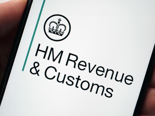 a person holding a phone, the screen is showing HMRC logo 