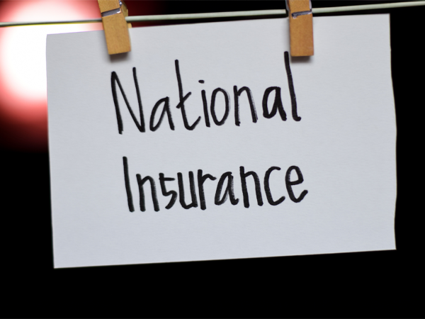 A wire with 2 wooden pegs holding a white sign with back text that reads 'NATIONAL INSURANCE' there is a black background with a singular circle of light to the left of the sign.