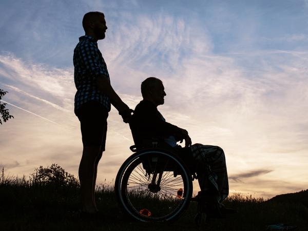 Image of the silhouette of a man pushing another man in a wheelchair