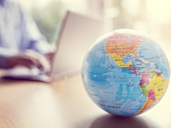 Person typing an a laptop with a globe in the foreground. ©istock/BrianAJackson