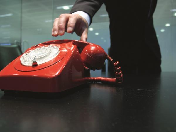 A hand reaching for a red telephone.