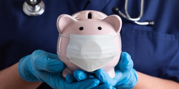 a medical professional wearing scrubs and blue gloves, holding a piggy bank. 