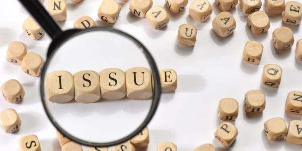 wooden letter blocks scattered around, a magnifying glass showing blocks that read the word 'ISSUE' 