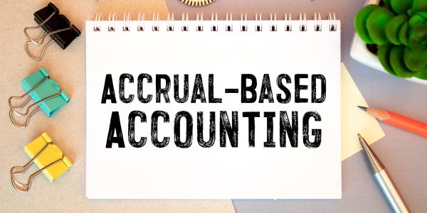 A pad of white paper with the words 'ACCRUAL-BASED ACCOUNTING' around the pad of paper various stationary can be seen. 