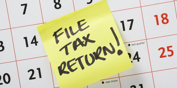 a calendar with a sticky note attached, note says in back ink 'FILE TAX RETURN!'