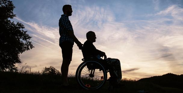 Image of the silhouette of a man pushing another man in a wheelchair Image of the silhouette of a man pushing another man in a wheelchair