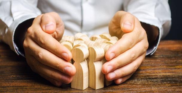 Image of a pair of hands surrounding wooden models of people illustrating job retention Image of a pair of hands surrounding wooden models of people illustrating job retention