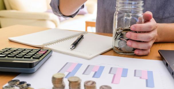 Image of a person counting coins surrounded by graphs and a calculator Image of a person counting coins surrounded by graphs and a calculator