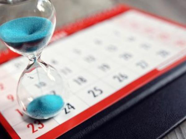 a red and white calendar with an hour glass on top of it, the hourglass has blue sand running through it.