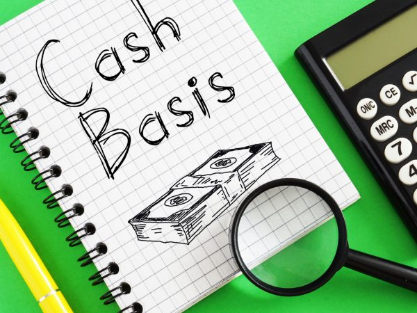 a calculator, a magnifying glass and a pad of squared paper with the words 'Cash basis' written on the top sheet along with an illustration of a stack of money