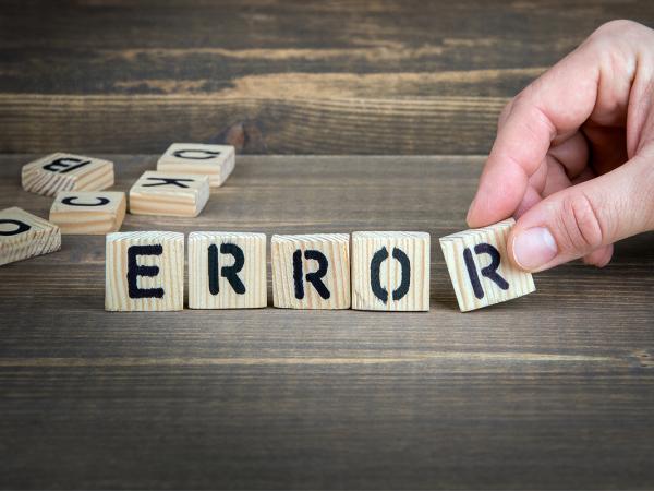 A person arranging homemade wooden scrabble tiles to spell the word 'ERROR'