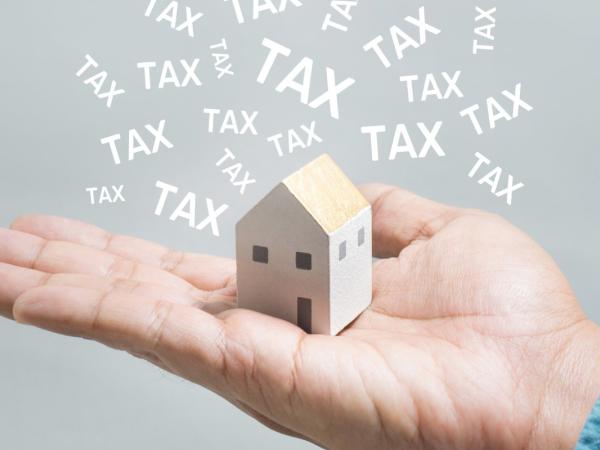 a person holding a small wooden house in the palm of their hand with the word 'TAX' surrounding it.