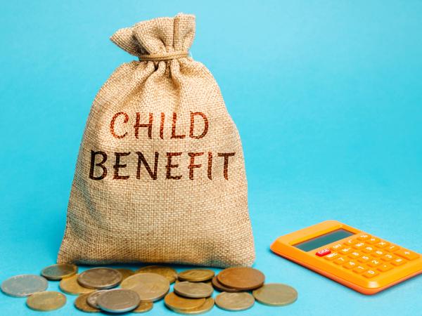 A burlap sack, an orange calculator and a scattering of coins against a blue background. On the sack the words 'CHILD BENEFIT' are written.