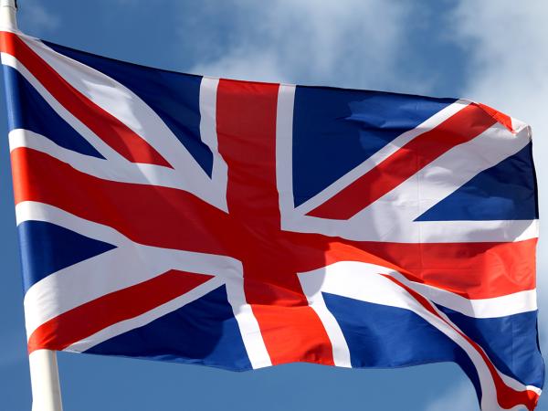 A flag of the United Kingdom blowing in the breeze, a blue sky is in the background.