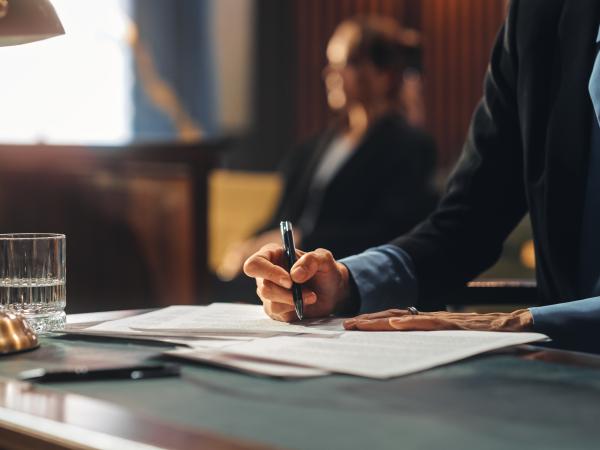 person writing on a document in an official room