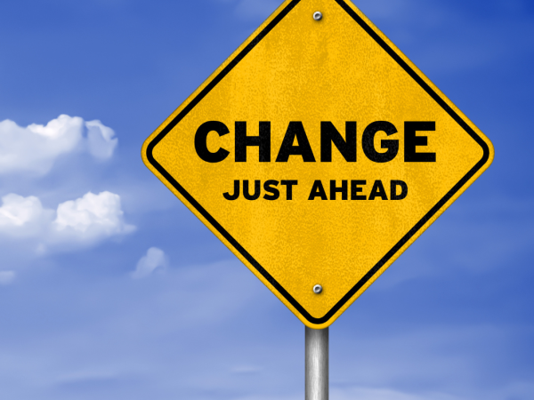 Yellow road sign with black lettering 'CHANGE JUST AHEAD' background of a blue sky with few white clouds 