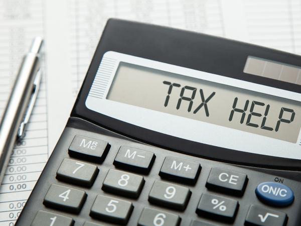 a calculator and a silver pen, the calculator showing the words 'TAX HELP' 