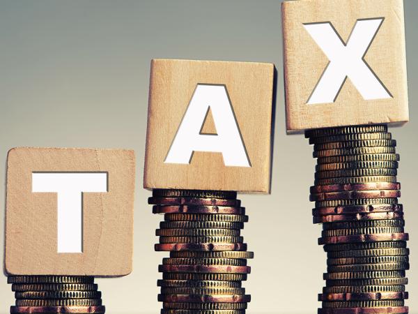 3 piles of coins with a wooden block on top of each pile, each block has a letter on it, together they spell the word 'TAX' 