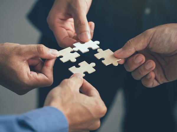 Four people each holding a piece of jigsaw puzzle together, each piece will fit into the next perfectly. 