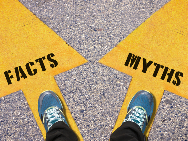 a person stood with one foot each on a yellow arrow one pointing left with the word 'FACTS' written on it, the other pointing right with the word 'MYTHS' written on it 