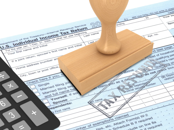 paper tax return with a calculator and a wooden stamper, the words 'TAX REFUND' are stamped on the page