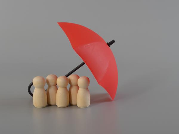 5 small wooden figures huddled underneath a small red umberella