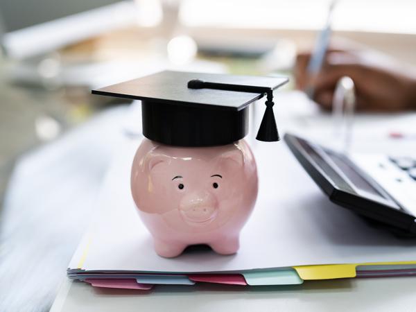 a piggy bank wearing a graduation cap and a person working at a desk