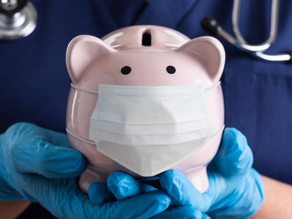 a medical professional wearing scrubs and blue gloves, holding a piggy bank. 