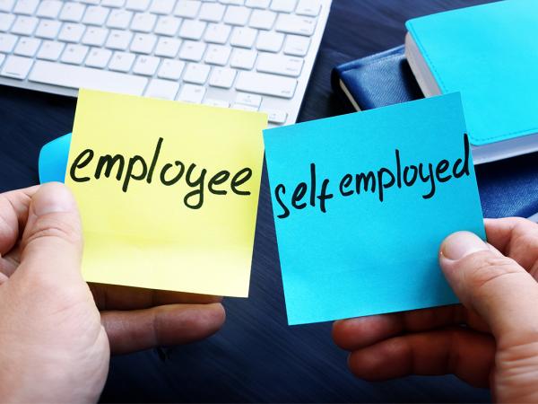 a person sat at a desk holding 2 post-it notes, one says 'EMPLOYEE' and the other 'SELF EMPLOYED' 