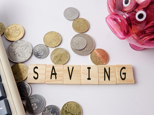 wooden tiles spelling out 'SAVING' next to a calculator, and a piggy bank, coins are scattered around the wooden tiles