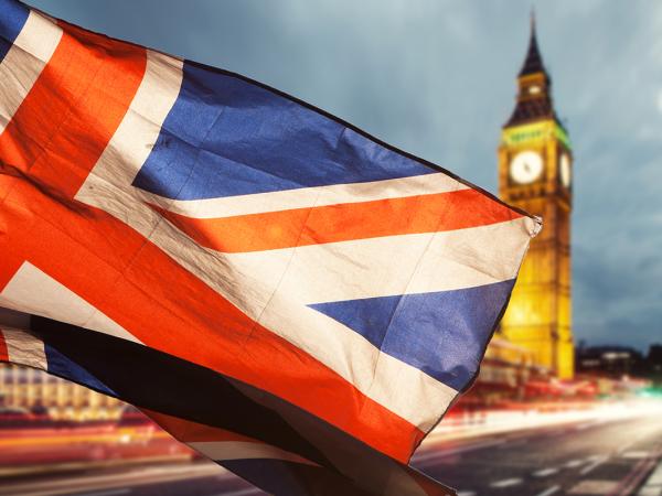 London at evening time, Big Ben can be seen and a flag of the United Kingdom is blowing across the image