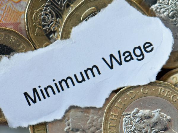 a pile of coins and a small scrap of paper with the words 'MINIMUM WAGE' typed in black ink. 