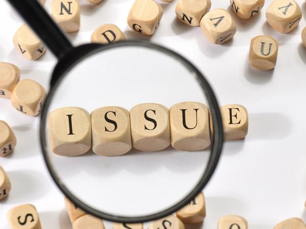 wooden letter blocks scattered around, a magnifying glass showing blocks that read the word 'ISSUE' 