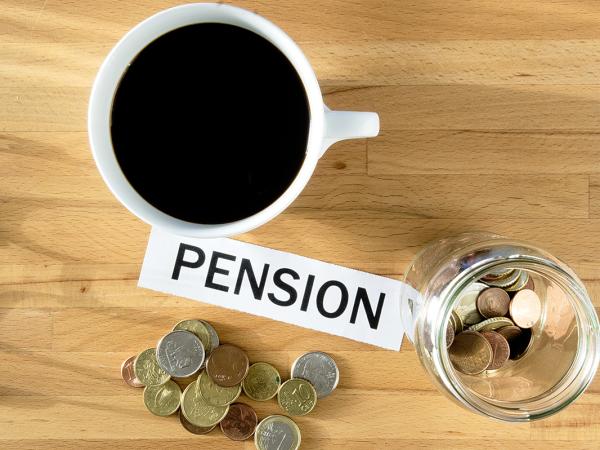 a birds eye view of a table top with a jar of coins, pen, coffee, glasses, loose coins and a piece of paper with the word 'PENSION' in black ink.  
