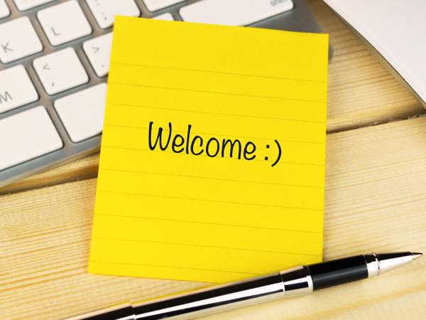 a yellow post-it note with the word 'WELCOME' written on it along with a smiley face. next to the post-it note is a pen and a keyboard.