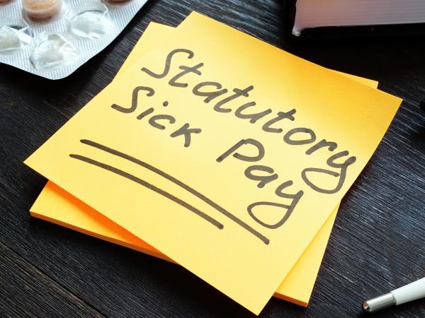 a yellow post-it note with the words 'STATUTORY SICK PAY' in black writing, next to this is a black marker pen, a thermometer and a pack of tablets. 