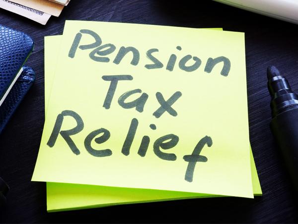 a post-it note against a dark coloured desk that reads 'PENSION TAX RELIEF' next to this is a leather folder, a pair of glasses and a black marker pen. 