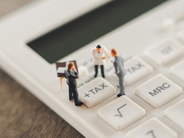 Tiny confused people stood on a calculator, huddled around the '+TAX' button 