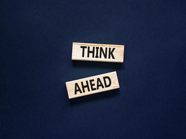 A dark coloured background with 2 wooden blocks, each block has a word written on it, together this reads 'THINK AHEAD' 