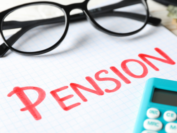 a pad of paper with the word 'PENSION' written on it with red ink, a calculator and a pair of glasses. 