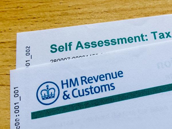 2 sheets of paper on a wooden table, laid on top of each other but slightly overlapping, these are letters from HMRC the front letter shows the HMRC logo in the top left corner, the one behind shows the words 'SELF ASSESSMENT: TAX CALCULATION'