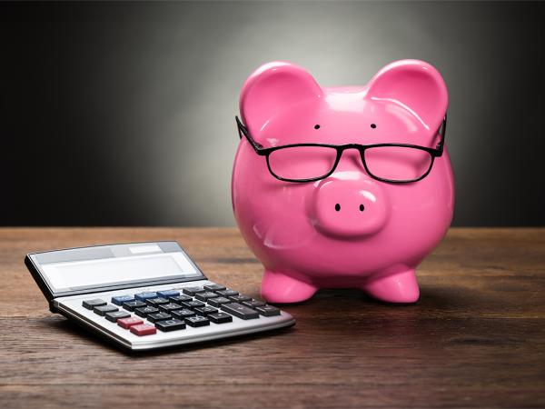 a pink piggy bank wearing glasses, sat next to a calculator. 