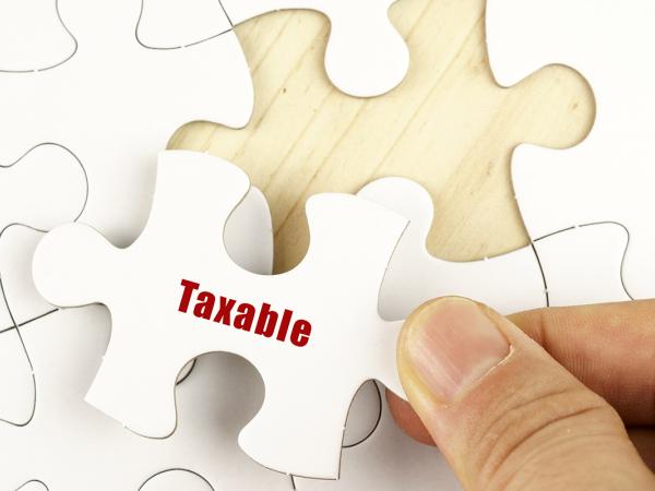 a white jigsaw on a wooden table with only one piece left to place, the final piece has the word 'TAXABLE' on it in red text. 