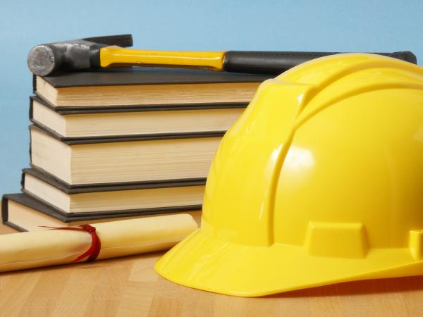 a desk with various books, a rolled up scroll and a construction hat.  