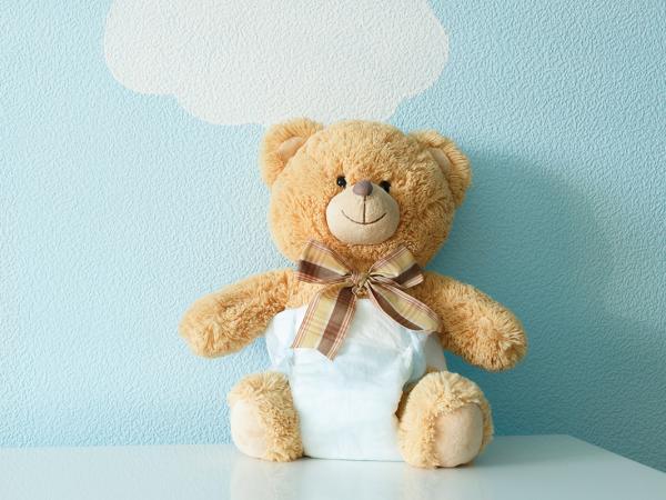 a teddy bear wearing a nappy against a pale blue painted wall with images of white clouds painted on. 