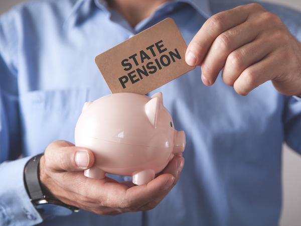 a person holding a piggy bank and inserting a card with the words 'STATE PENSION' into the piggy bank