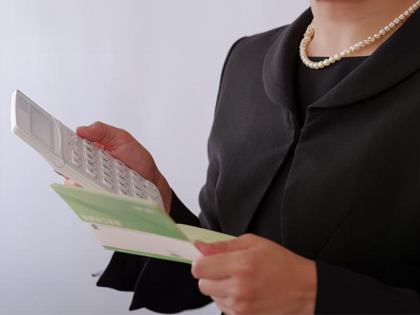 a person reading through documents, holding a calculator. The person is wearing black clothing and a pearl necklace. 