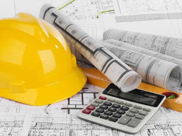 background is made up of construction drawings, on top of those sit a construction hat, rolled up plans, a calculator and a spirit level. 