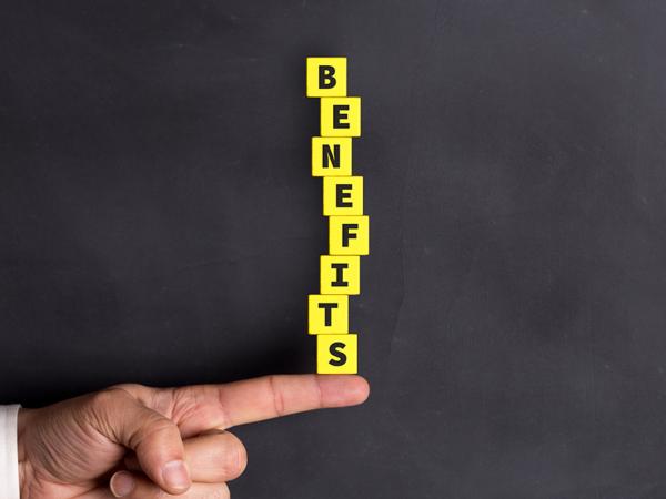 a person balancing yellow blocks on their finger, the blocks each have a letter written on them together spelling the word 'BENEFITS'