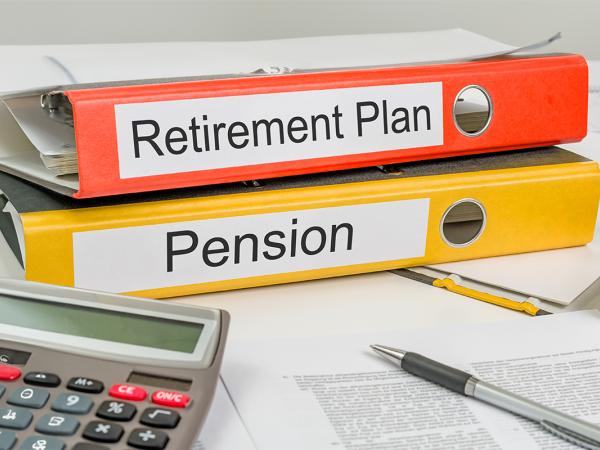 a desk with scattered paperwork, a calculator and 2 folders, written on the spines of the folders are the words 'PENSION' and 'RETIREMENT PLAN'